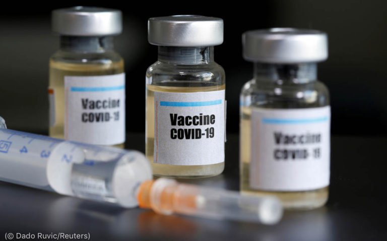 Small bottles labeled with a "Vaccine COVID-19" sticker and a medical syringe are seen in this illustration